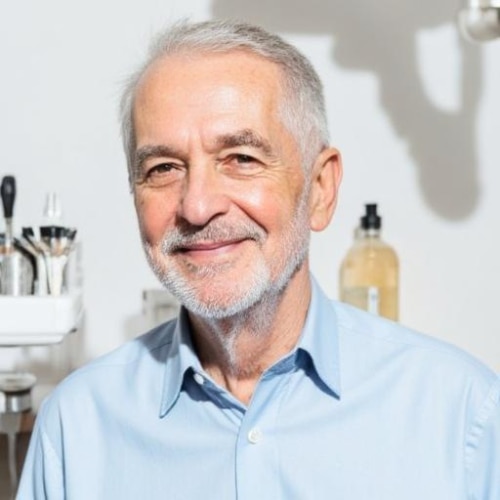 Smilende ældre herre med gråt skæg og blå skjorte i lyse omgivelser hos en tandlæge